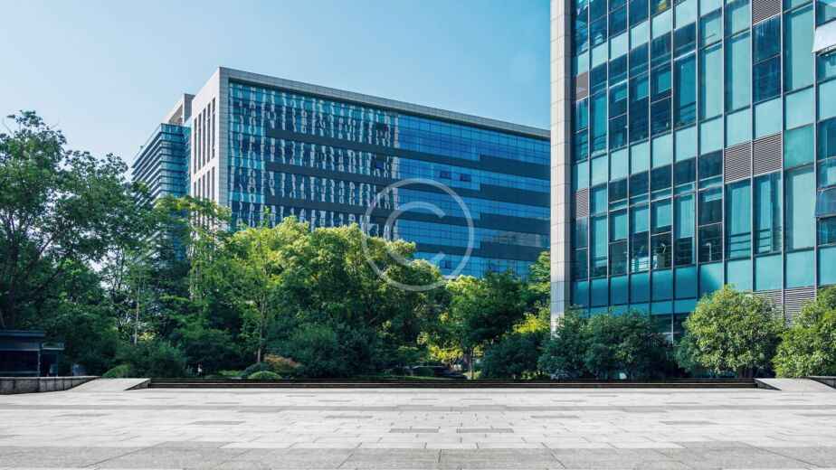Modernos edificios de oficinas con fachadas de cristal, rodeados de árboles y una plaza abierta pavimentada bajo un cielo azul despejado, ponen de manifiesto la pericia de un hábil contratista de proyectos a la hora de crear espacios urbanos acogedores.