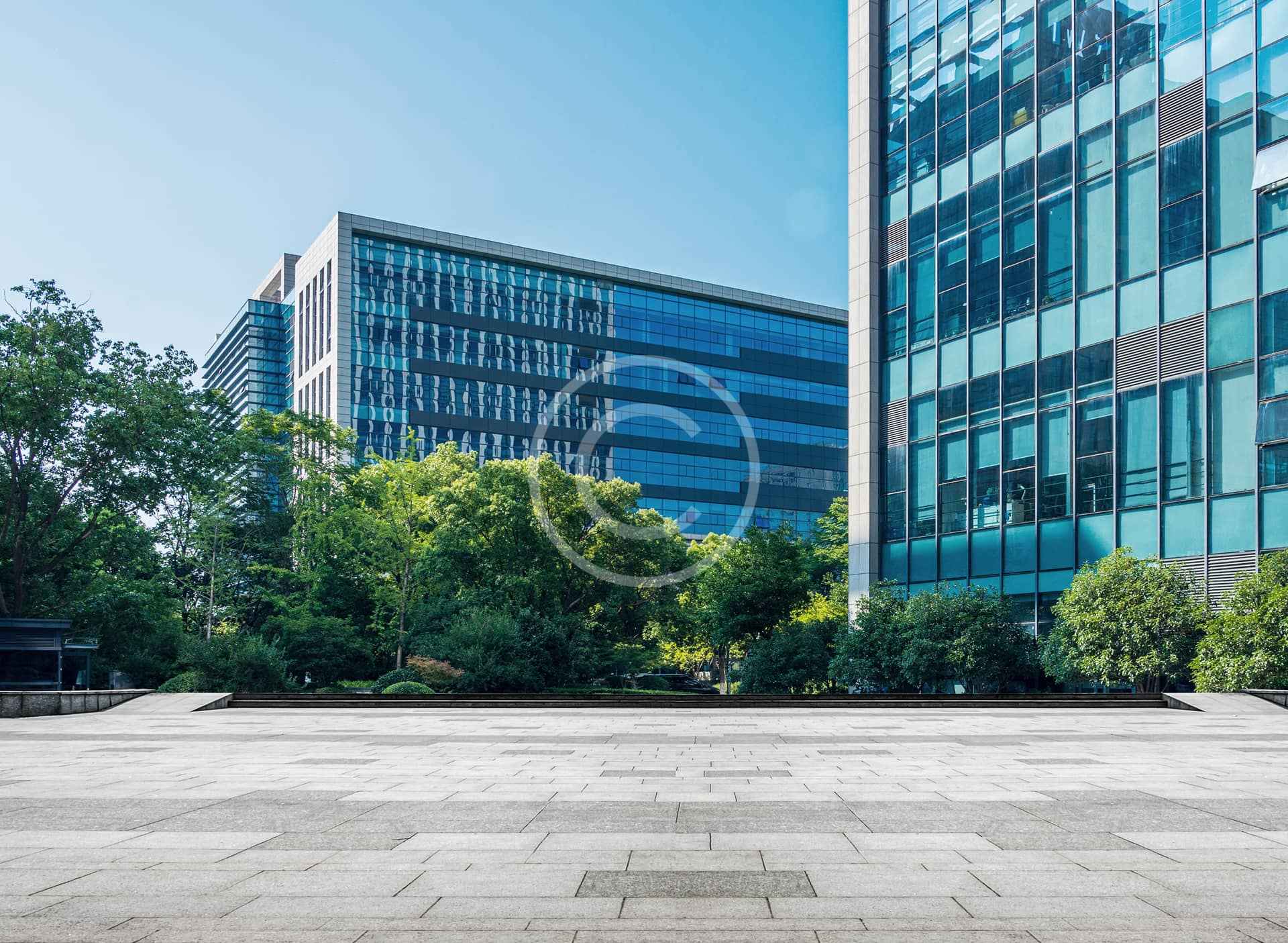 Modernos edificios de oficinas con fachadas de cristal, rodeados de árboles y una plaza abierta pavimentada bajo un cielo azul despejado, ponen de manifiesto la pericia de un hábil contratista de proyectos a la hora de crear espacios urbanos acogedores.