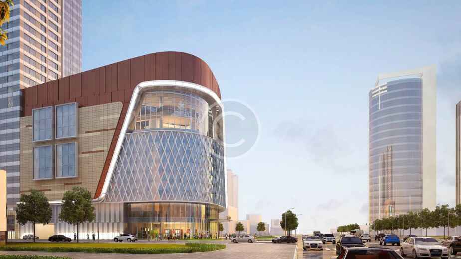 Calle de una ciudad moderna en la que se ve un edificio de cristal curvado, posiblemente de construcción prefabricada, con torres de gran altura al fondo y coches aparcados a lo largo de la calzada.