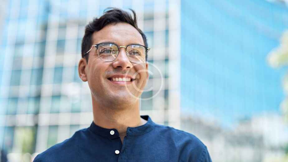 Un hombre con gafas y camisa azul oscuro sonríe de pie frente a un moderno edificio de cristal, reflejo de la evolución del diseño de viviendas y de la construcción moderna.