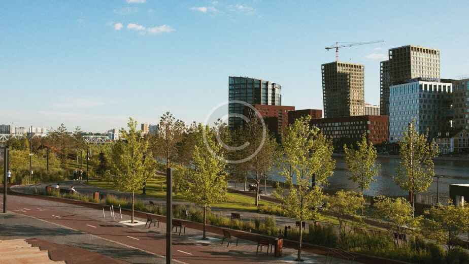 Paisaje urbano con modernos rascacielos de construcción sostenible, un río y un parque con árboles y senderos bajo un cielo azul despejado.