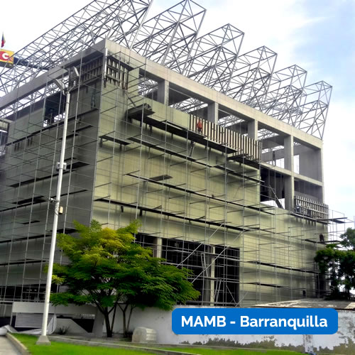 Un edificio moderno en construcción con andamios en su fachada y armazón metálico encima; rotulado "MAMB - Barranquilla" en la esquina inferior derecha.