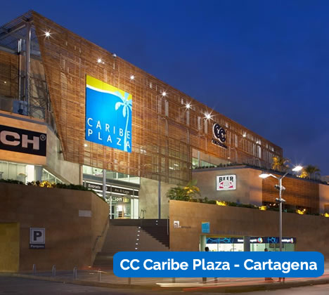 Vista exterior del centro comercial CC Caribe Plaza de Cartagena al atardecer, con letreros luminosos y un diseño arquitectónico moderno.
