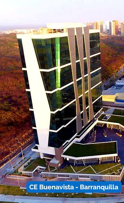 Un alto y moderno edificio de oficinas con ventanas de cristal, rodeado de vegetación y paisaje urbano, rotulado "CE Buenavista - Barranquilla".