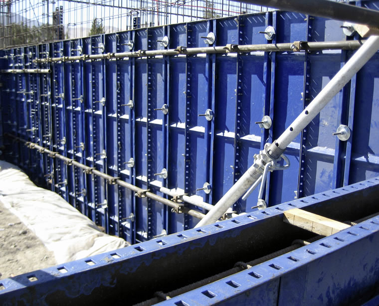 Paneles de encofrado de acero azul para muros y tirantes metálicos colocados en una obra, preparados para el vertido del hormigón.