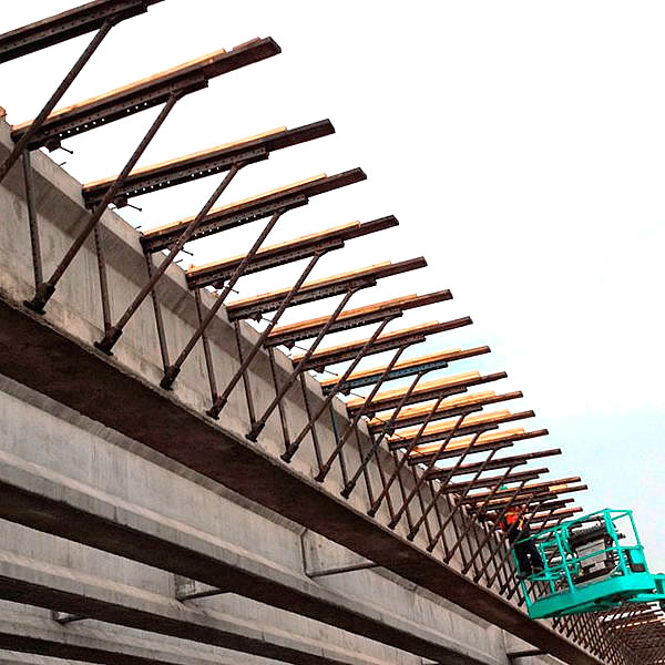 Un trabajador de la construcción maneja un ascensor junto a la estructura de hormigón de un puente con vigas de soporte en ángulo y tablones de madera instalados a lo largo del borde superior.
