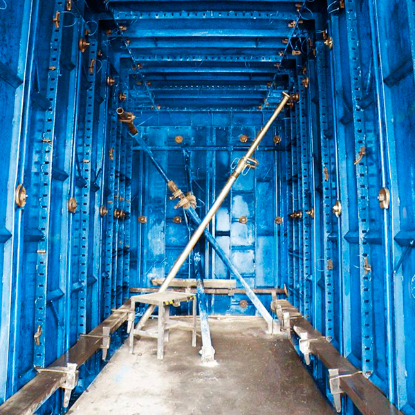 Una estructura metálica rectangular pintada de azul con varias barras de soporte y andamios en su interior, vista desde un extremo hacia el otro.