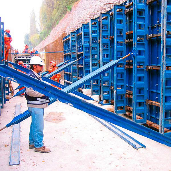 Trabajadores de la construcción montan encofrados de acero azul en una obra, preparándose para el vertido del hormigón. Los trabajadores llevan equipo de seguridad, incluidos cascos y chalecos.