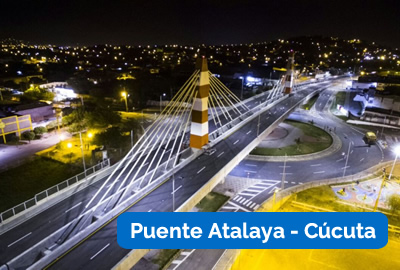 Vista aérea nocturna de Puente Atalaya, un puente atirantado en Cúcuta, Colombia, iluminado por farolas con las luces de la ciudad al fondo.