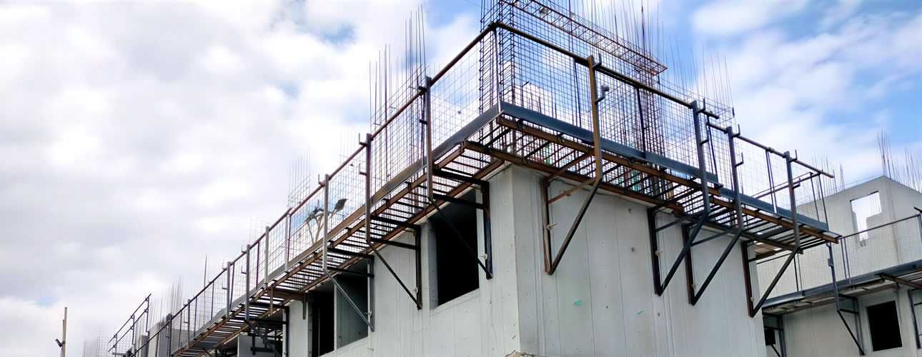 Un edificio de hormigón de varios pisos en construcción con varillas de acero a la vista, andamios y armazones contra un cielo nublado.