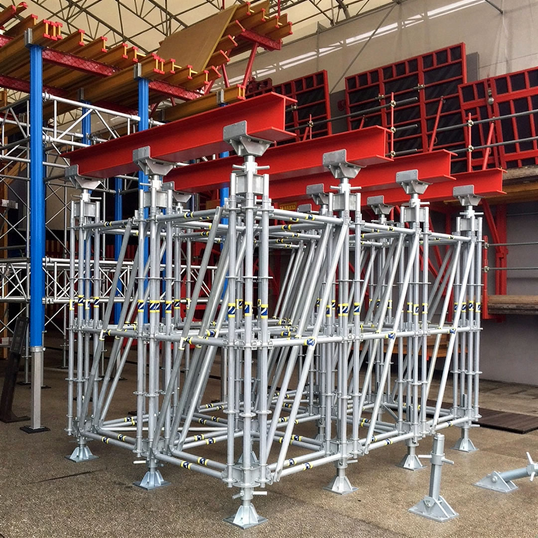 Una estructura modular de andamio de acero con vigas en I rojas en la parte superior se instala en el interior, rodeada de otros materiales de construcción y componentes de andamiaje.