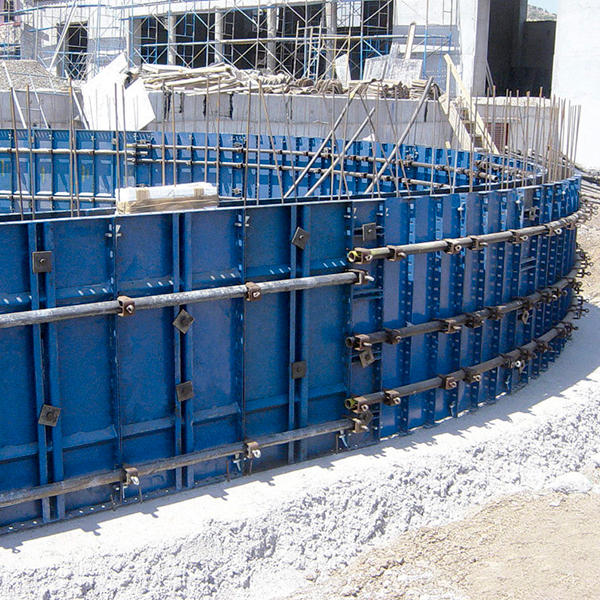 Encofrado metálico azul colocado en forma circular en una obra, con andamios y materiales de construcción visibles al fondo.