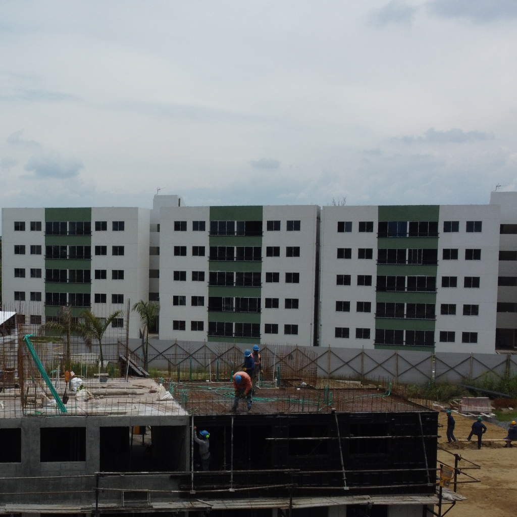 Varios obreros construyen un edificio con encofrados Unispan en primer plano, mientras que al fondo, bajo un cielo nublado, se ven edificios de apartamentos blancos ya terminados.