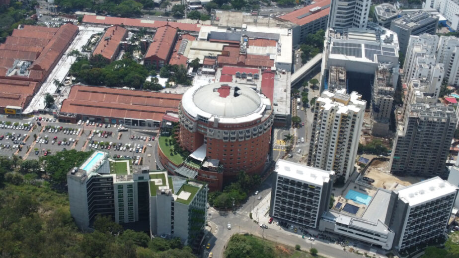 Vista aérea de un paisaje urbano con edificios altos, una estructura central circular, aparcamientos y vegetación circundante. En primer plano se ve una colina. El logotipo de UNISPAN, abajo a la derecha, destaca las soluciones del Sistema Industrializado.