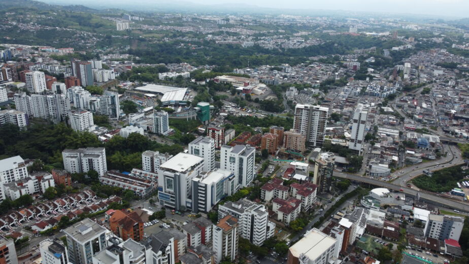 Vista aérea de una ciudad de Colombia con edificios densamente apiñados, apartamentos de gran altura, carreteras, zonas verdes y estructuras encofradas que se extienden en la distancia bajo un cielo nublado.
