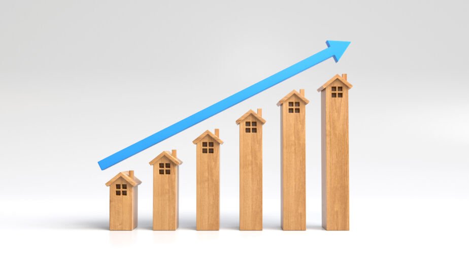 Seis maquetas de casas de madera dispuestas en orden ascendente de altura, con una flecha azul que apunta hacia arriba sobre ellas, lo que simboliza el crecimiento o las tendencias al alza en el sector de la vivienda, el mercado inmobiliario o la tasa hipotecaria.